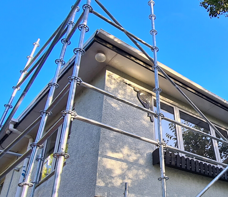 Grey two story house wrapped in silver scaffolding with blue sky in the background